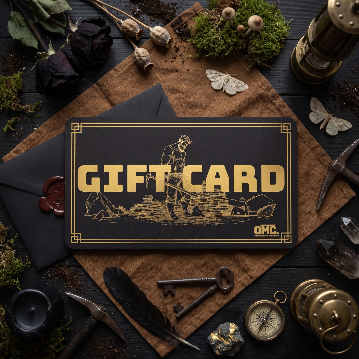 OMC gift card in black with gold foil miner artwork, overhead flat lay on brown linen